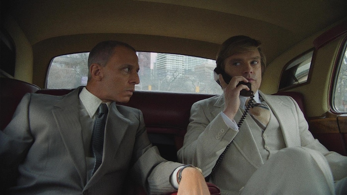Deux hommes à l'arrière d'une voiture, l'un étant au téléphone.