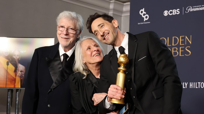 Elliott Broidy, Sylvia Plachy et Adrien Brody, qui tient un trophée en souriant, la tête penchée.