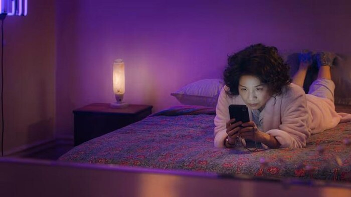 Une femme couchée sur un lit regarde son téléphone portable.