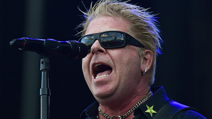 Dexter Holland porte des lunettes fumées et chante dans un micro. 