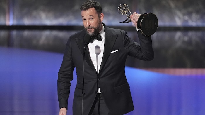 Noah Wyle sur scène avec un trophée dans les mains.