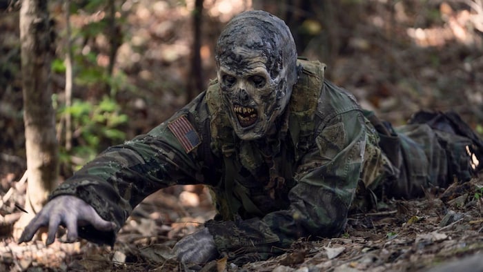 Un zombie en tenue de soldat américain rampe sur le sol dans la forêt. 