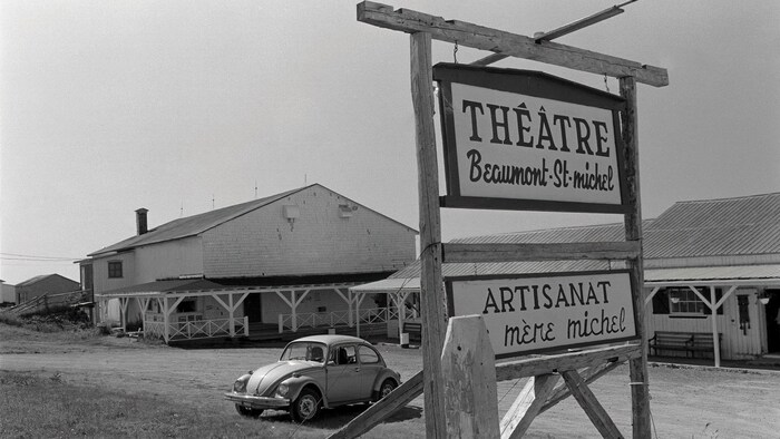 Pancarte qui annonce le théâtre avec la grange et une voiture.