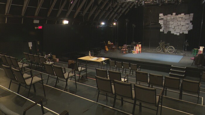 Des chaises distanciées devant une scène de théâtre.