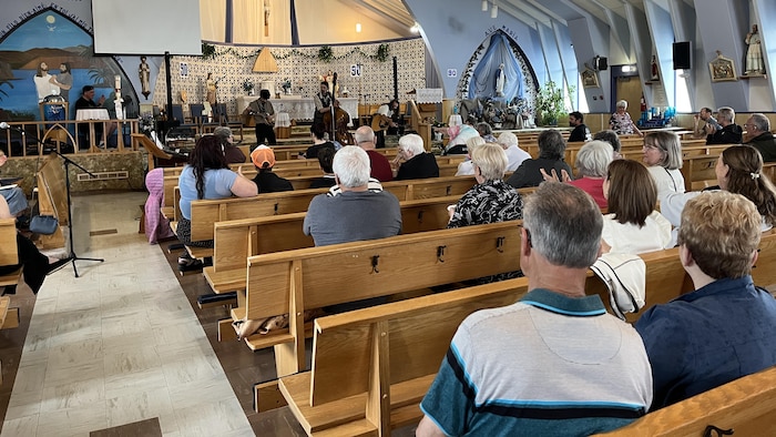 Quelques dizaines de personnes sont assises dans des bancs d'église pour écouter le groupe Les Gringalets.