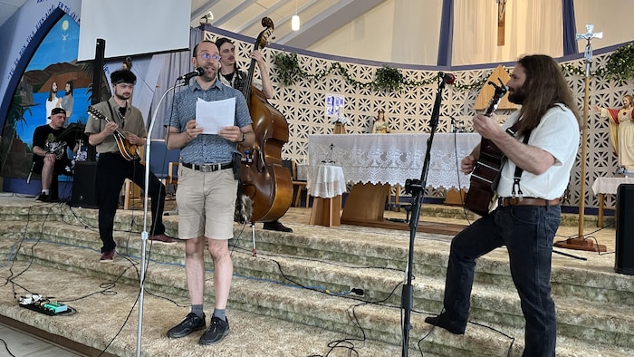 Guillaume Beaulieu parle au micro pendant que le groupe Les Gringalets joue de la musique à l'église de Mont-Brun.