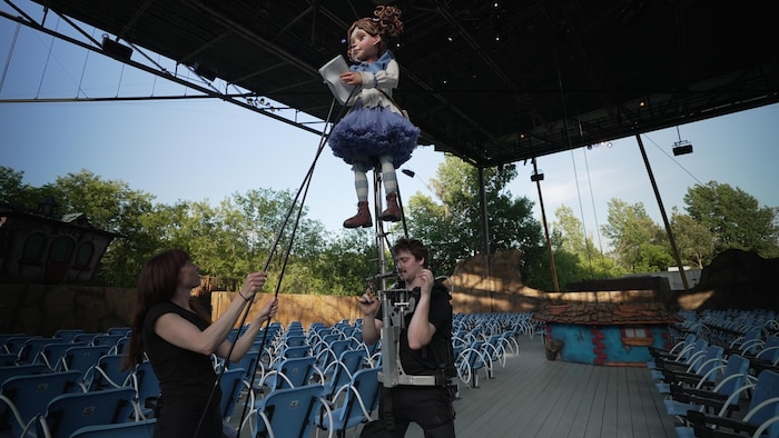 Dans une salle de théâtre vide, Élise Lessard-Mercier et Vincent Lachance manipulent un système qui permet de faire bouger une marionnette géante.