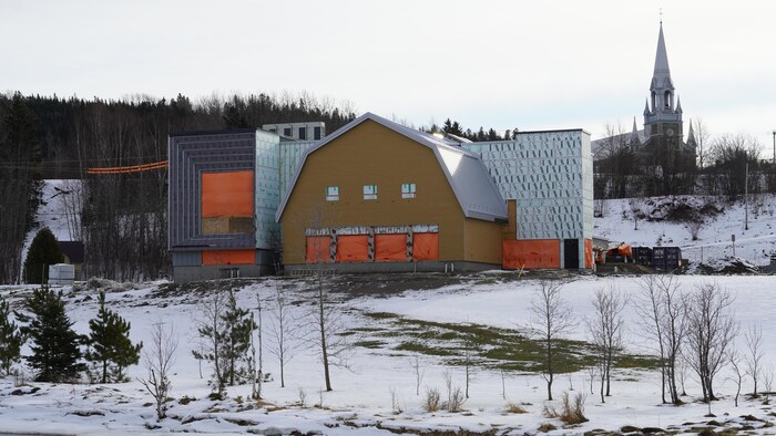 Le théâtre est en chantier : le revêtement extérieur n'est pas encore installé. Derrière la bâtisse, il y a la façade de l'église du Bic.