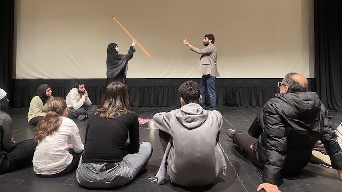 Une femme voilée lance un long bâton à un homme sur scène.