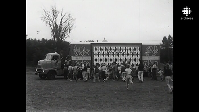 Le camion-remorque transportant le théâtre La Roulotte est  entouré d'enfants.