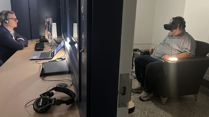 Un homme porte un casque de réalité virtuelle et le médecin est de l'autre côté d'une vitre.