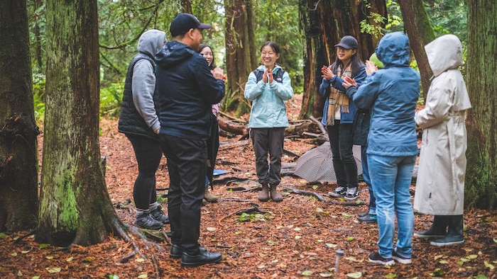 Des participants à un atelier de thérapie par la forêt sont regroupés en cercle avec le professeur Guangyu Wang dans la forêt.