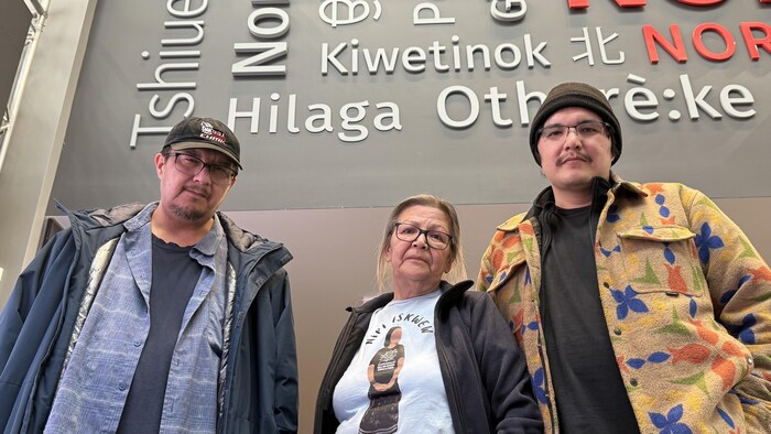 Thérèse Ottawa, Anthony Dubé et Alexandre Nequado dans l'atrium de Radio-Canada, devant un mur sur lequel est écrit Nord en langues autochtones.