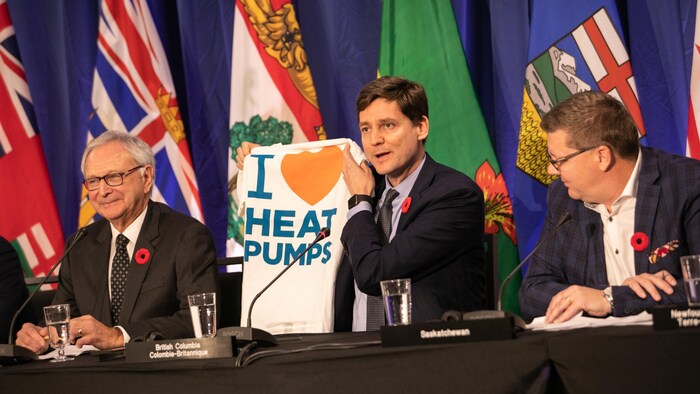 David Eby, premier ministre de la Colombie-Britannique, prend la parole lors d'une conférence de presse lors de la réunion du Conseil de la Fédération à Halifax. Il tient un tee-shirt disant « J'aime les thermopompes ».