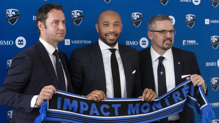 Trois hommes tiennent une écharpe sur laquelle est écrit Impact de Montréal.