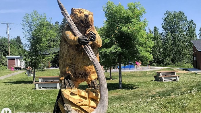 Une grande sculpture d'un castor qui tient un arbre.
