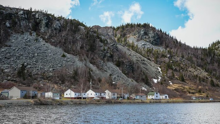 Quelques maisons sur le rivage devant des collines rocheuses.