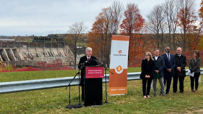 Tim Hodgson donne une conférence de presse devant un barrage hydroélectrique.