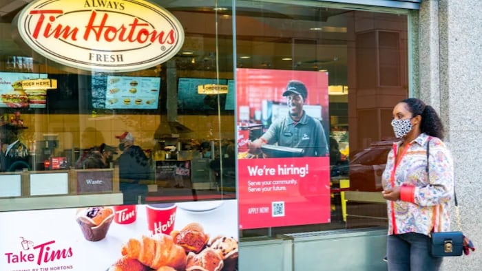 A woman walks past a Tim Hortons. Employees work there.