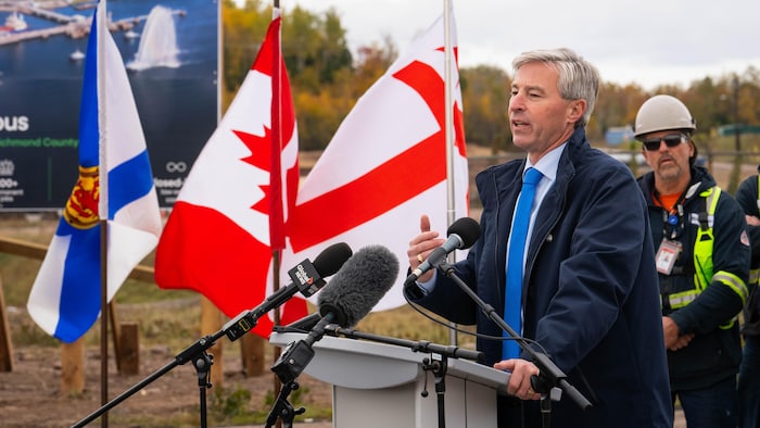 Le profil gauche de Tim Houston, debout devant des micros lors d'une conférence de presse en plein air, près d'une grosse pancarte avec les mots «Point Tupper Data Centre Campus».