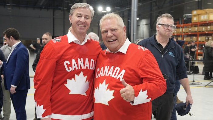 Tim Houston et Doug Ford sont debout et posent ensemble, vêtus de chandails de hockey rouge aux couleurs du Canada.