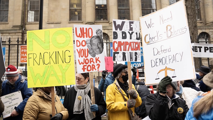 Des personnes qui manifestent en hiver. Plusieurs affiches sont levées, dont une sur laquelle on a écrit «No Fracking Way» et une autre avec le visage de Tim Houston et la question «Pour qui travailles-tu?»