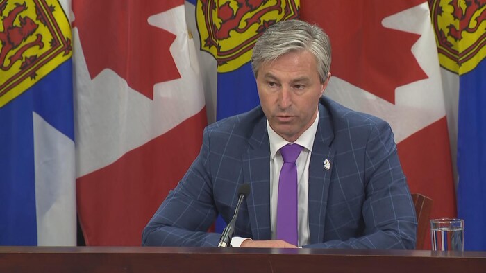 Tim Houston est assis à un micro devant des drapeaux du Canada et de la Nouvelle-Écosse.