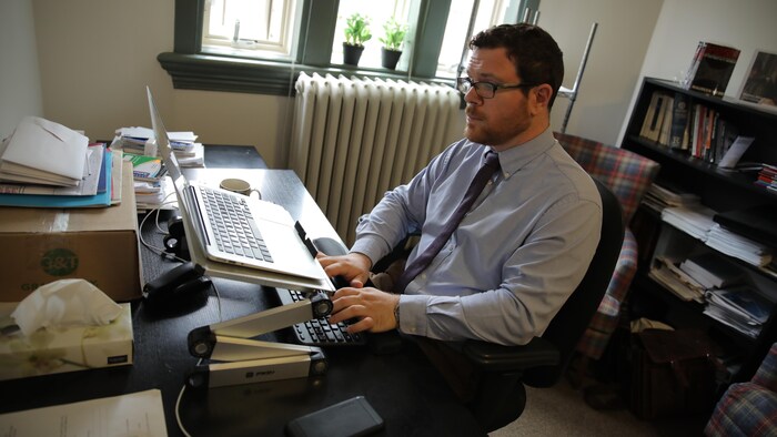 Tim McSorley est assis dans son bureau devant son ordinateur portable ouvert et près d'une fenêtre.