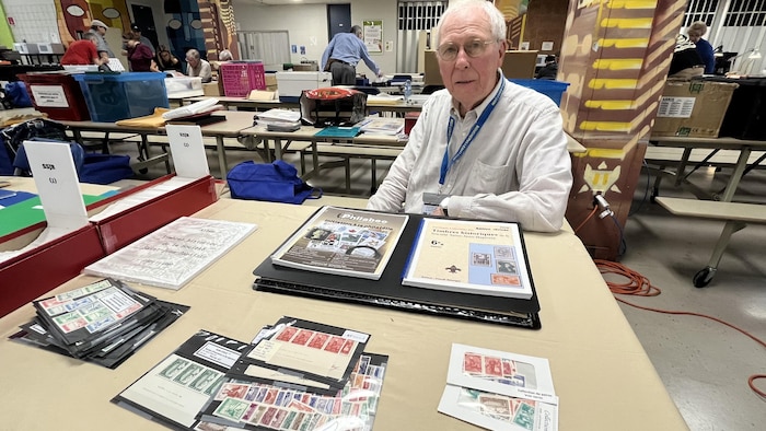 Claude Bélanger pose devant d'anciens numéros de la revue Philabec et des timbres.