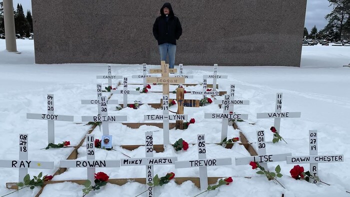 Des croix blanches sont plantées dans la neige avec des roses et le nom des défunts.