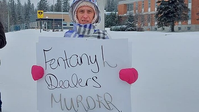 Louise Lefebvre tient une pancarte antidrogue dehors l'hiver devant un poste de police.
