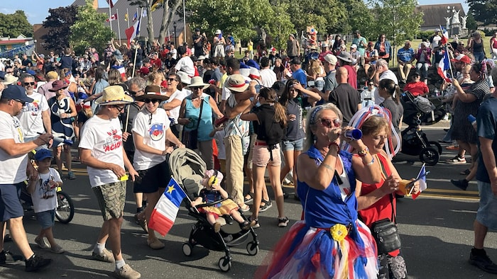Des gens défilent dans la rue. Une femme costumée à l'avant souffle dans une trompette en plastique.