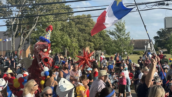 Un dragon rouge en papier mâché coiffé d'un chapeau pointu avance au milieu d'un défilé.