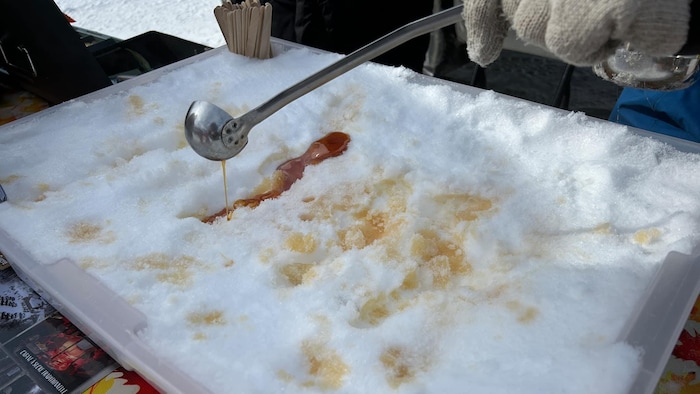 Une personne fait couler du sirop d'érable sur de la neige à l'aide d'une louche.