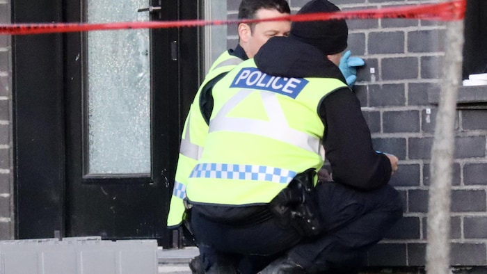 Deux policiers regardent les impacts de balles dans un mur.