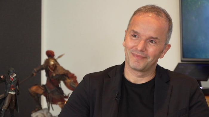 Un homme sourit devant des statuettes de personnages de jeux vidéo.