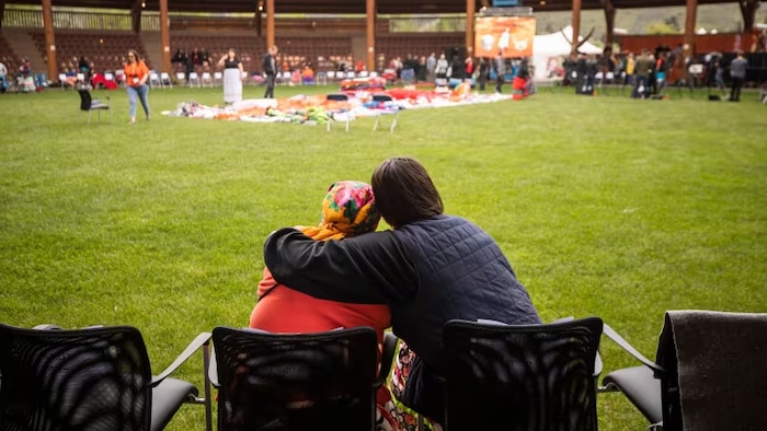 Deux personnes assises se font un câlin en regardant les événements liés aux commémorations.