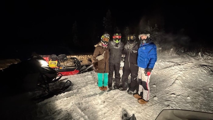 Quatre membres d'une famille en hiver, entourée de motoneiges.