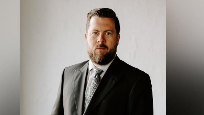 Austin Corbett sits on the corner of a table and stares at the camera.