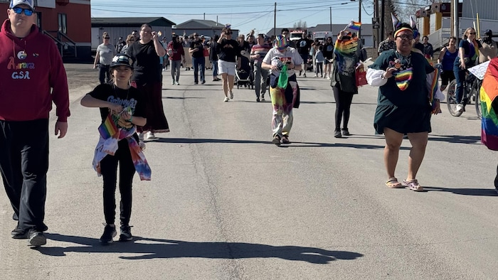 Des gens défilent dans la rue d'un village, arborant les couleurs arc-en-ciel de la Fierté