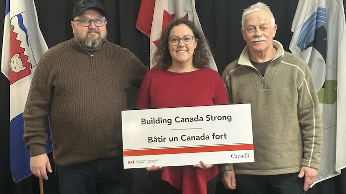 Rebecca Alty tient une pancarte qui dit « Bâtir un Canada fort » aux côtés de Denny Rodger et Peter Clarkson