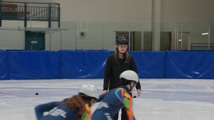 Des patineurs de vitesse s'entraînent sur la glace devant leur entraîneuse.
