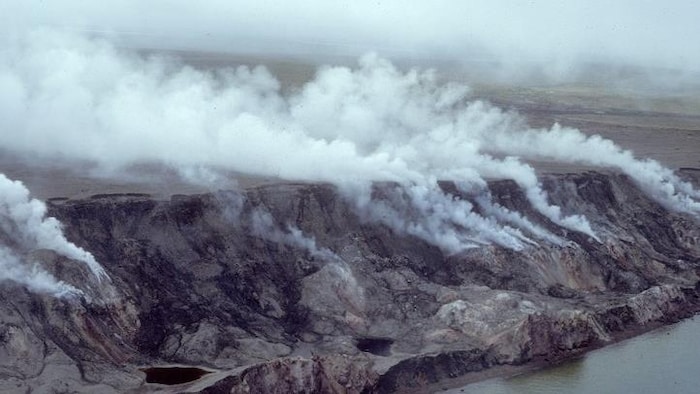 Une fumée blanche s'élève au-dessus d'une falaise avec de l'eau en contrebas.