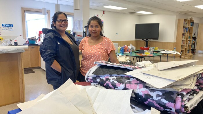 Felicia Beaulieu est debout à côté de sa fille Hannah dans une pièce remplie de tissus et de patrons de couture lors d'un atelier de fabrication de parka traditionnel dans la communauté de Behchoko, aux Territoires du Nord-Ouest, en août 2022. 