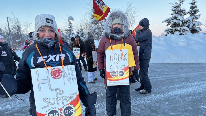 Deux personnes dehors en hiver, avec des affiches qui disent, en anglais, honk for support, le 8 février 2023, à Yellowknife.