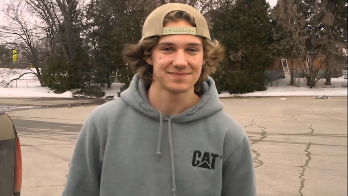 Tobin Spiers porte un chandail à capuchon avec une casquette et est debout au milieu d'un parc de stationnement.