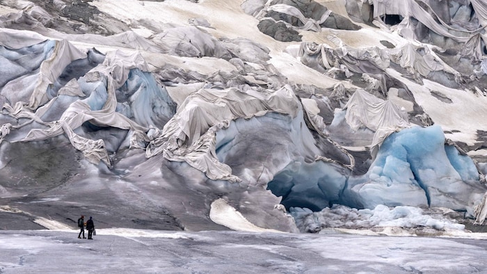 Men in front of a glacier partially covered with white canvases.