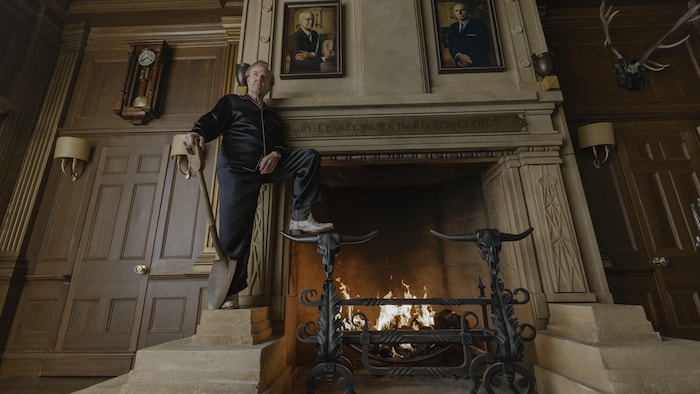 Un homme se tient debout devant un grand foyer, une pelle dans la main.
