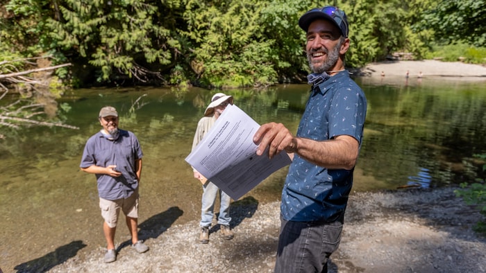 Tom Gleeson tient un papier dans la main, près d'une rivière.