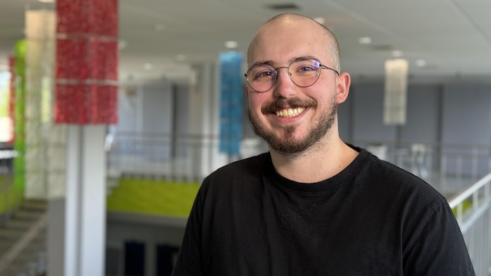 Un étudiant chauve avec des lunettes sourit à l'objectif.